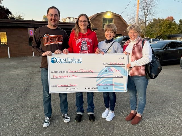 Employees present a donation to two local high schools during a rivalry football game